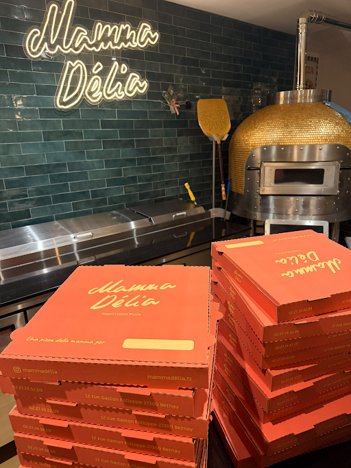Four à pizza doré et enseigne néon Mamma Délia dans la pizzeria de Bernay